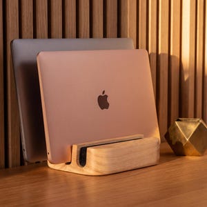 a wooden stand holding two laptops, one silver and one gold, with a geometric sculpture placed next to them on a wooden desk.
