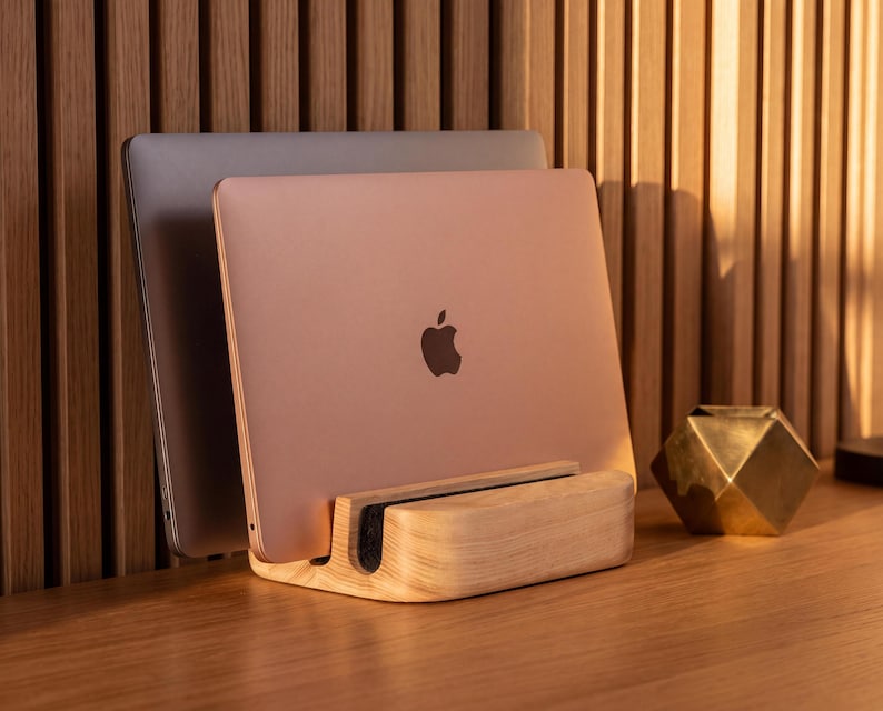 a wooden stand holding two laptops, one silver and one gold, with a geometric sculpture placed next to them on a wooden desk.
