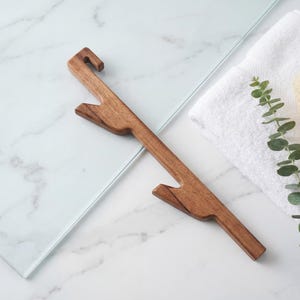 a wooden object, possibly a tool or utensil, placed on a marble surface alongside a white towel and some greenery.