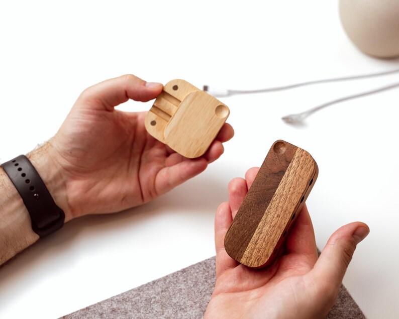 A person's hands holding two wooden objects, one of which appears to be a small wooden box or organizer, while the other is a wooden object with a similar shape.
