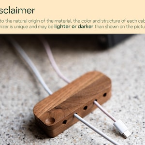a wooden cable organizer with multiple white cables plugged into it, placed on a speckled surface.