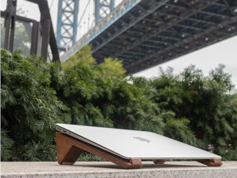 an apple laptop sitting on a ledge under a bridge