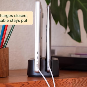 two laptops connected to a charging station, with a wooden desk and a plant in the background.