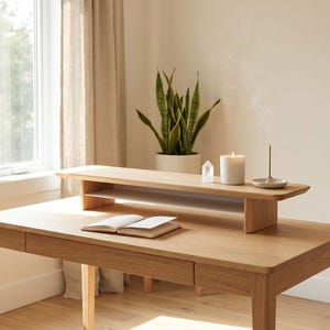 a wooden desk with a book, a candle, and a plant, situated in a room with a window and a curtain.