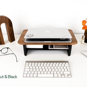 a workspace with a laptop, glasses, a keyboard, and a mouse on a white desk. There is also a wooden stand and a vase with orange flowers.