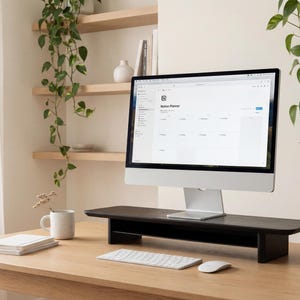 a well-organized workspace with a computer monitor, keyboard, and mouse on a wooden desk. The monitor displays a calendar application, and there are some plants and decorative items in the background.