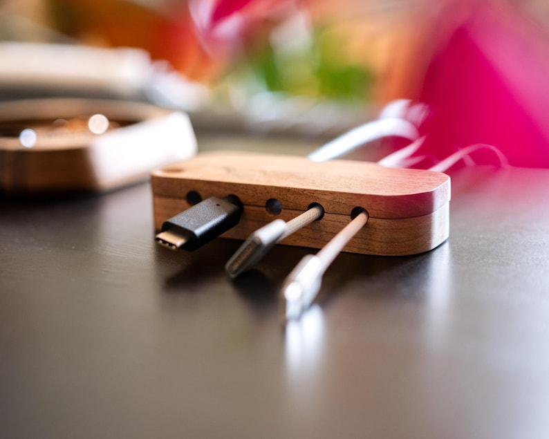 A wooden USB cable organizer with multiple USB cables neatly arranged inside it, placed on a wooden surface.