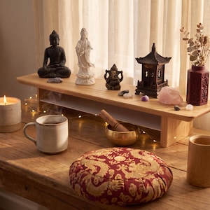 a wooden table with various objects arranged on it, including a cup, a bowl, a candle, a vase, a Buddha statue, and a dragon pillow.