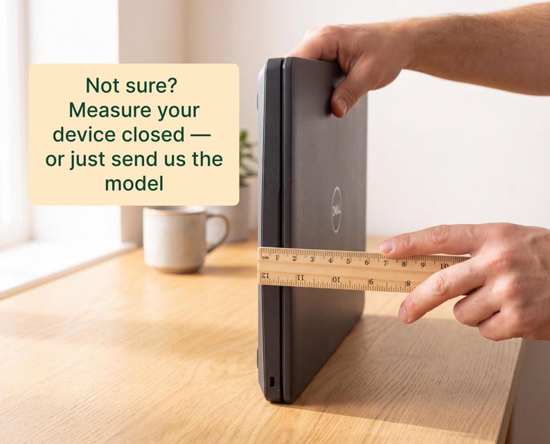 A person's hands are holding a ruler and measuring the size of a closed laptop computer on a wooden desk.