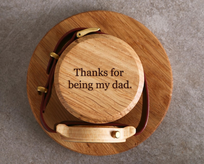 A wooden watch stand with a watch attached to it, and a message engraved on the watch stand that says "Thanks for being my dad."
