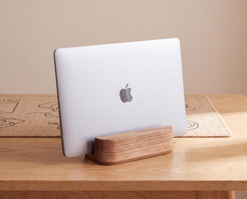 A white Apple laptop is sitting on a wooden stand on a wooden table.