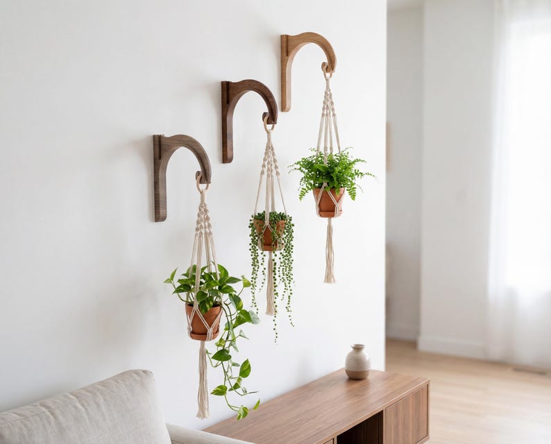 a cozy living room with a white wall and a wooden side table. Three hanging planters with various plants are displayed on the wall, creating a pleasant and natural atmosphere.