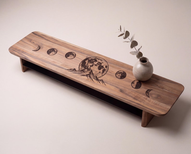 a wooden table with a decorative design depicting the phases of the moon, including the waxing and waning phases. A vase with greenery is placed on the table, adding a natural element to the scene.