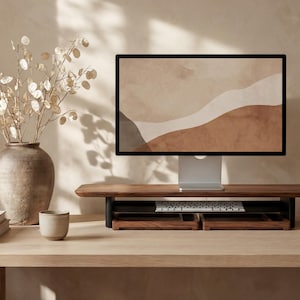 a wooden desk with a computer monitor, keyboard, and a vase with white flowers. The desk is set against a beige wall, and there is a cup and a book on the desk as well.