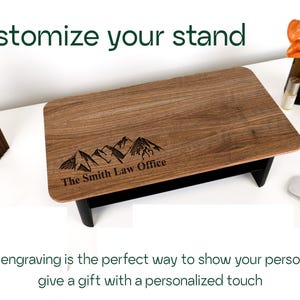 a wooden stand with a mountain design engraved on it, along with a wooden sculpture and a glass bottle. The text overlay encourages custom engraving as a way to showcase one's personality or give a personalized gift.