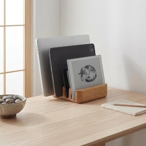 a wooden desk with a bowl of stones, a wooden stand holding three laptops, and a notebook.