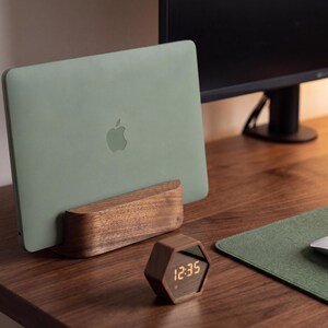a wooden desk with a green Apple laptop on a wooden stand, a white mouse, and a wooden clock displaying 12:35.