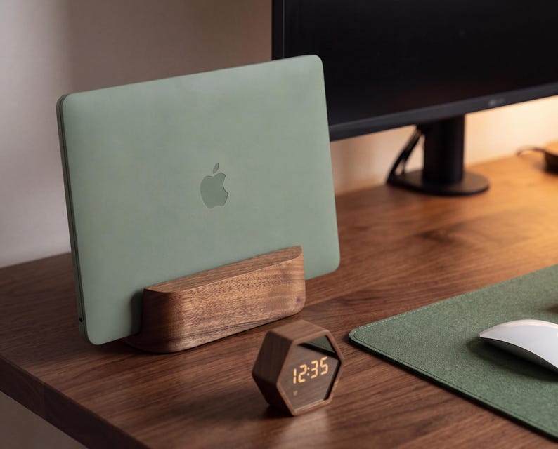a wooden desk with a green Apple laptop on a wooden stand, a white mouse, and a wooden clock displaying 12:35.