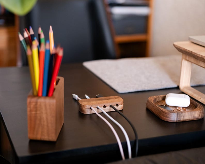 a wooden desk with various items on it, including a wooden pencil holder filled with colored pencils, a wooden tray with a white object, and a wooden charging station with multiple USB cables plugged into it.
