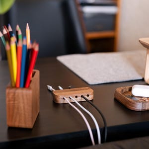 a wooden desk with various items on it, including a wooden pencil holder filled with colored pencils, a wooden tray with a white object, and a wooden charging station with multiple USB cables plugged into it.