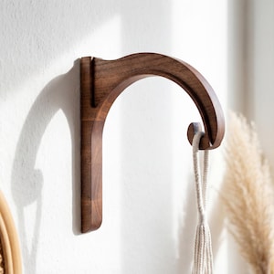 A wooden hanging hook is mounted on a white wall, with a woven basket visible in the background.