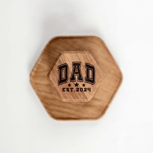 A wooden hexagonal object with the text "DAD EST. 2024" engraved on it.