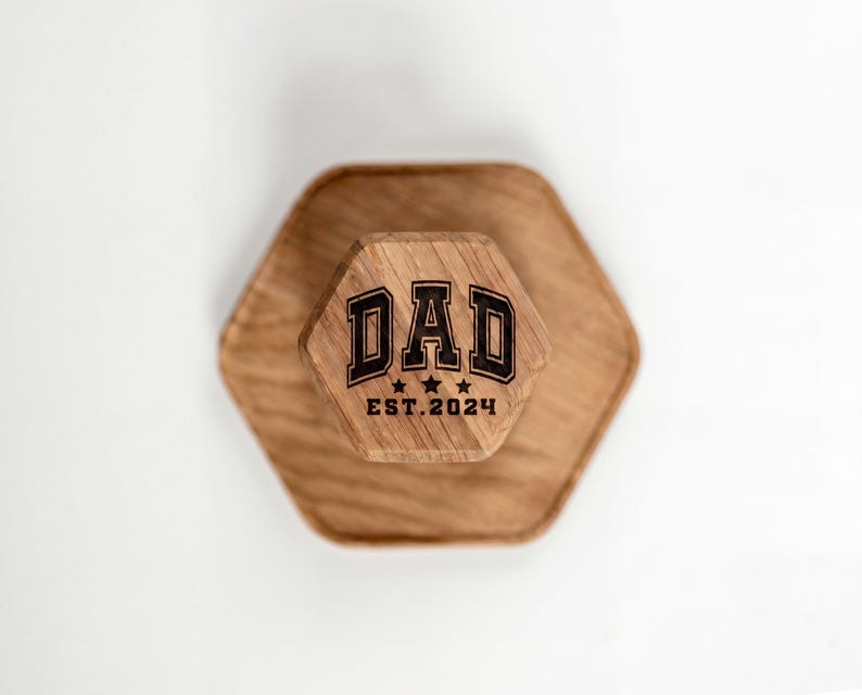 A wooden hexagonal object with the text "DAD EST. 2024" engraved on it.