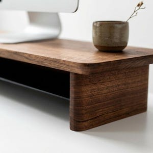 a wooden desk with a computer monitor, a small ceramic cup, and a plant on the desk.