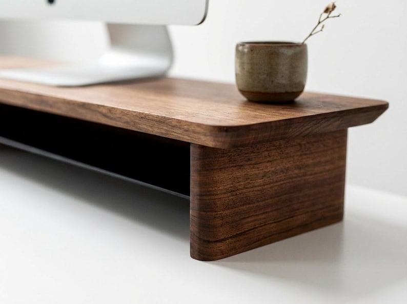 a wooden desk with a computer monitor, a small ceramic cup, and a plant on the desk.