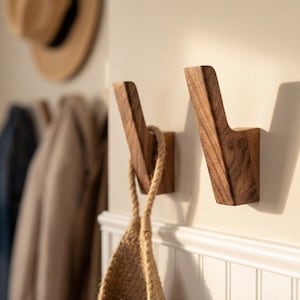 a wooden coat rack with two hooks mounted on a wall, holding coats and a hat.