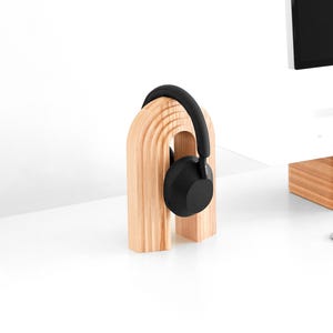 May include: A wooden headphone stand shaped like an arch with a black pair of headphones resting on it.