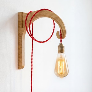 A wooden light fixture with a red cord hanging from it, and an illuminated light bulb attached to the cord.
