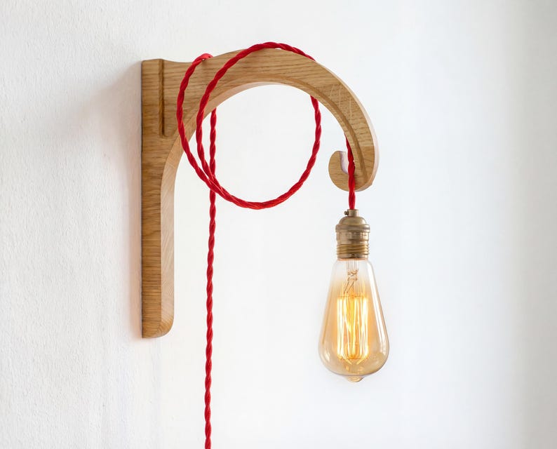 A wooden light fixture with a red cord hanging from it, and an illuminated light bulb attached to the cord.