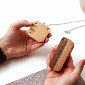 A person's hands holding two wooden objects, one of which appears to be a small wooden box or organizer, while the other is a wooden object with a similar shape.