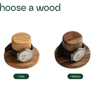 two wooden watch holders, each with a watch placed on top. The watch holder on the left is made of oak, and the one on the right is made of walnut.