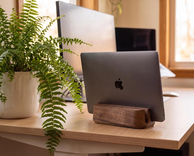 a wooden stand holding a laptop, with a potted plant and a computer monitor in the background.