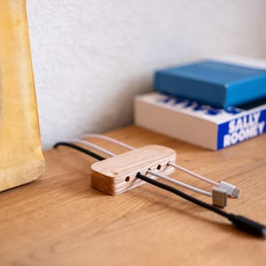 a wooden charging station with multiple USB cables plugged into it, placed on a wooden surface next to a stack of books.