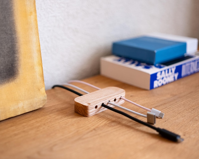a wooden charging station with multiple USB cables plugged into it, placed on a wooden surface next to a stack of books.