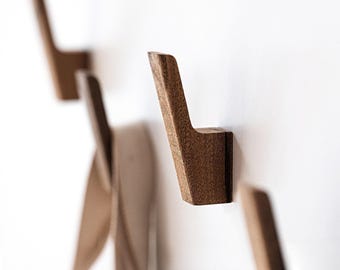May include: A set of wall-mounted coat hooks crafted from dark brown wood with a visible grain. Each hook features an angled, upward-pointing design with a flat base that attaches directly to the wall surface, providing a sturdy support for items.