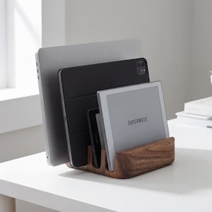 May include: A wooden desk organizer holds a silver laptop, a black tablet, and a gray tablet with the word "SUPERNOTE" on the screen. The organizer is made of dark wood and has multiple slots.