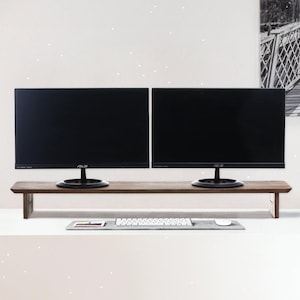 May include: A long, rectangular dark wood monitor stand with two black ASUS computer monitors placed on top. Below the stand, a white computer keyboard and a white computer mouse are positioned on a gray rectangular desk mat.