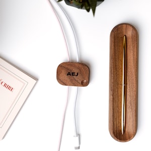 a wooden pen holder, a wooden cable organizer, a book, and a pen on a white surface.