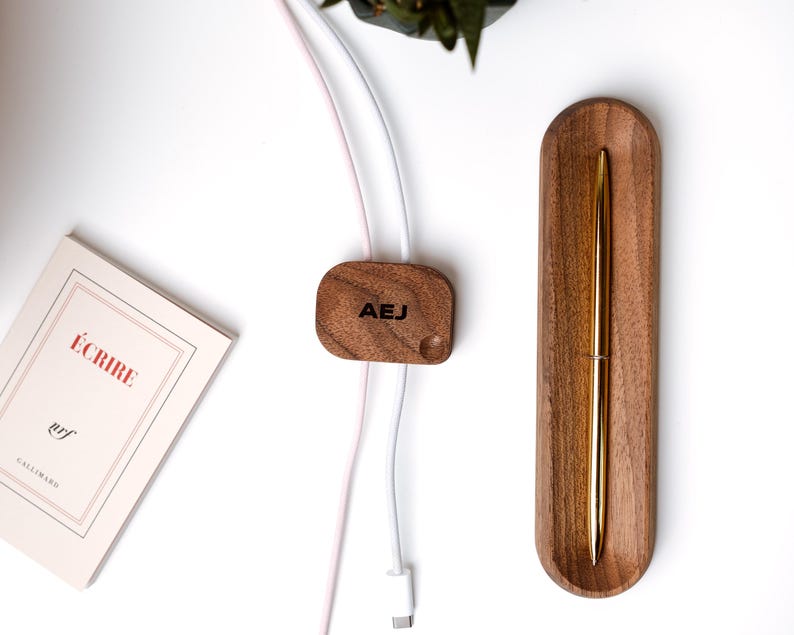 a wooden pen holder, a wooden cable organizer, a book, and a pen on a white surface.
