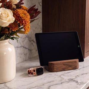 a tablet resting on a wooden stand, with a vase of white and orange flowers placed next to it on a marble countertop.