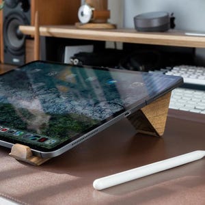 May include: A black tablet computer with a wooden stand and a white stylus on a brown surface. The tablet screen displays a variety of app icons.