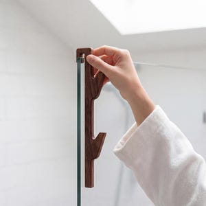 A person's hand is holding a wooden object, which appears to be a handle or a tool, in front of a glass door or window.