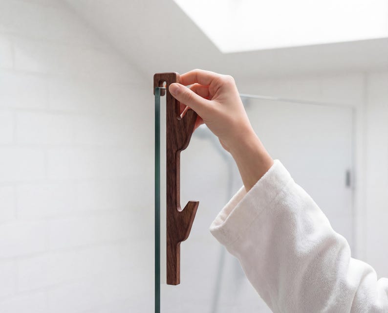 A person's hand is holding a wooden object, which appears to be a handle or a tool, in front of a glass door or window.