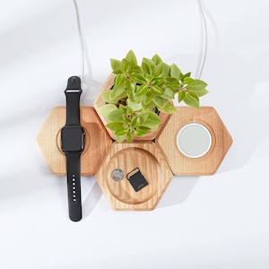 May include: A wooden hexagonal organiser featuring a black smartwatch, a small plant, a charging pad, a coin, and an SD card. The organiser is made of light-coloured wood and has a modern design. The smartwatch has a black strap.