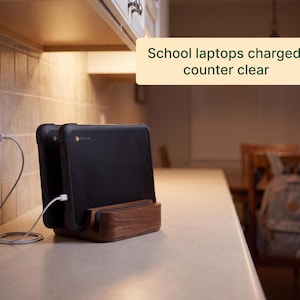 A kitchen counter with two school laptops charging, and a wooden charging dock holding the laptops.