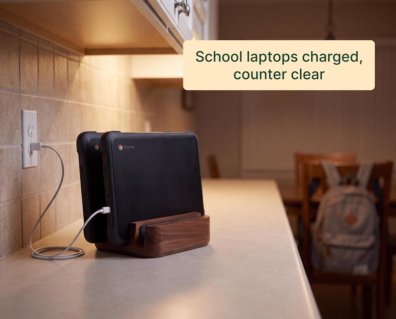 A kitchen counter with two school laptops charging, and a wooden charging dock holding the laptops.